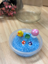 Load image into Gallery viewer, Blue pebbles, and pond figurines sitting on a timber bench, with a glass jar and mini plants in the background.
